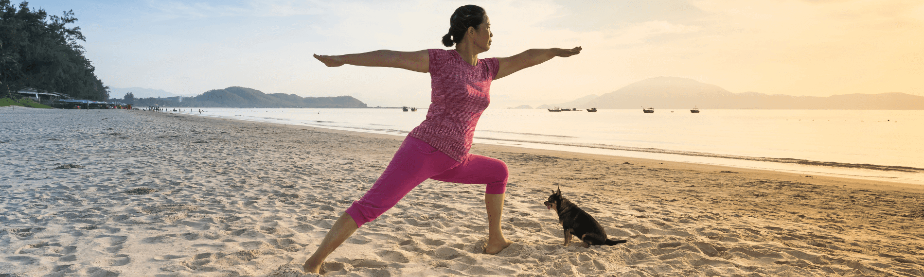 Woman doing yoga on beach with dog.